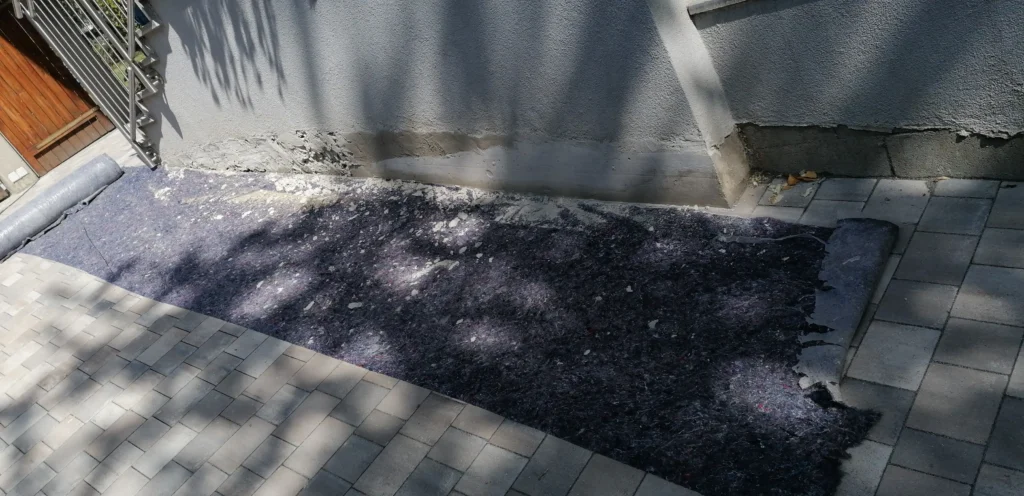 Sanierung im Sockelbereich mit Schutzvlies und vorbereiteter Pflasterfläche – Abdichtungsarbeiten