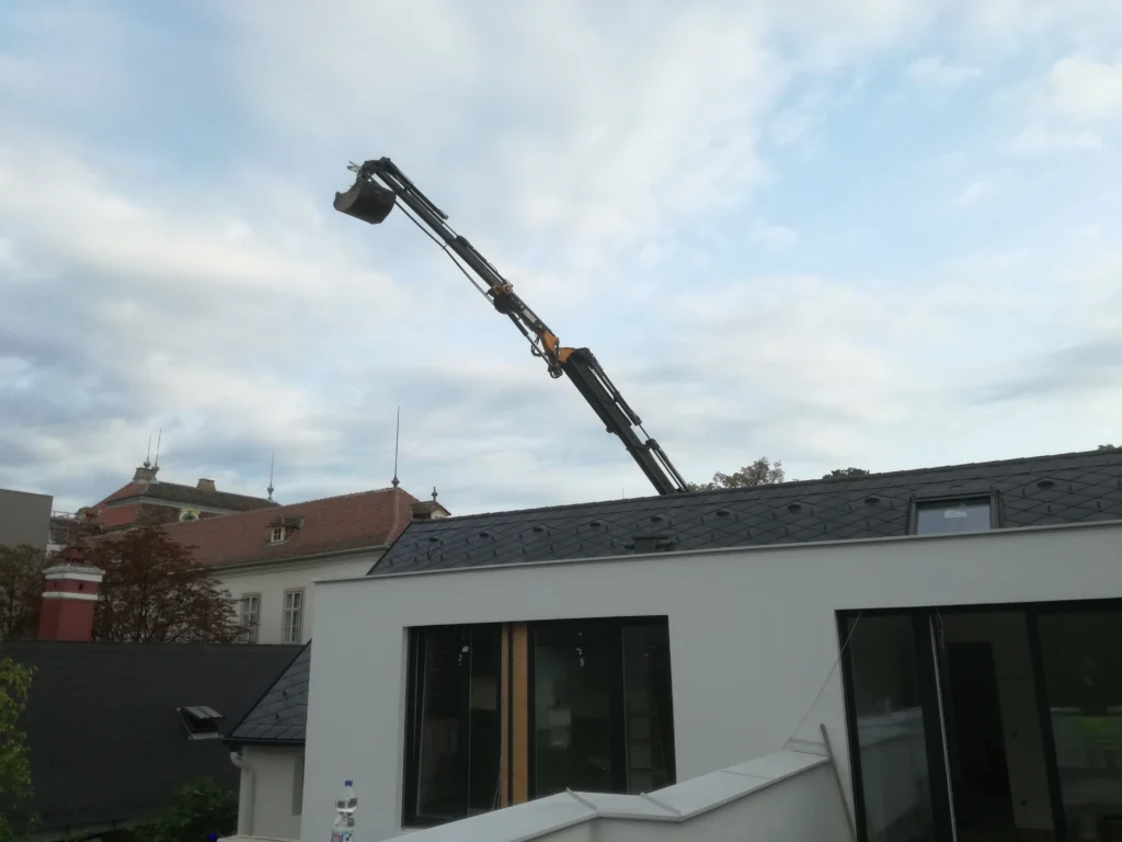 Bagger mit langem Ausleger über Hausdach – Spezialbaggerarbeiten bei schwer zugänglichem Gelände
